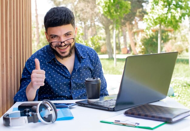 Feliz joven freelancer masculino levantando el pulgar mientras trabaja en la computadora portátil