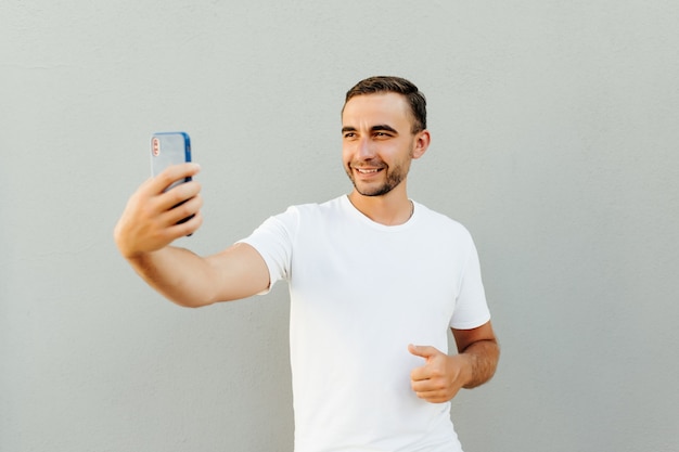 Feliz joven haciendo selfie aislado en pared gris