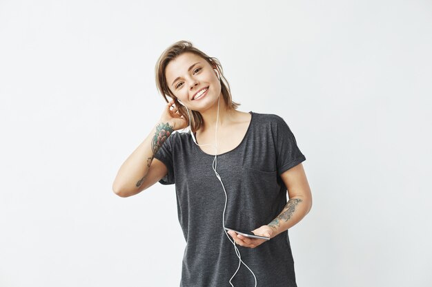 Foto gratuita feliz joven hermosa chica en auriculares con teléfono sonriendo.