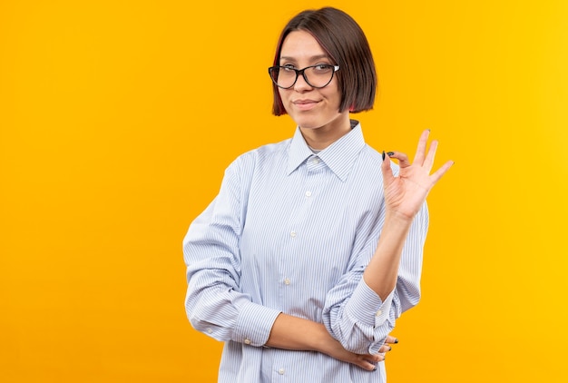 Feliz joven hermosa con gafas mostrando gesto bien aislado en la pared naranja con espacio de copia