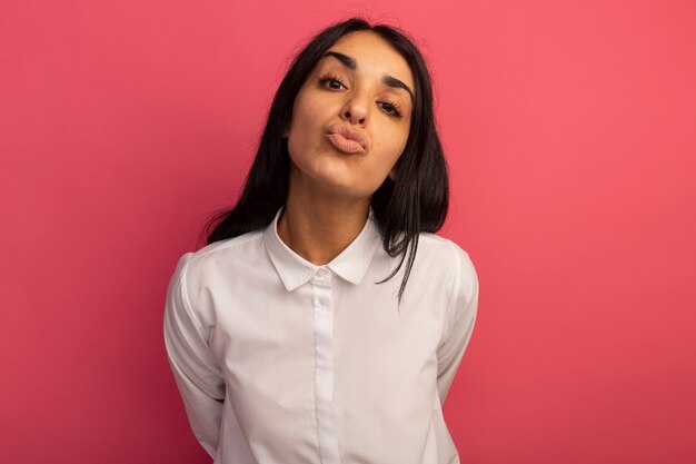 Feliz joven hermosa vestida con camiseta blanca mostrando gesto de beso aislado en rosa