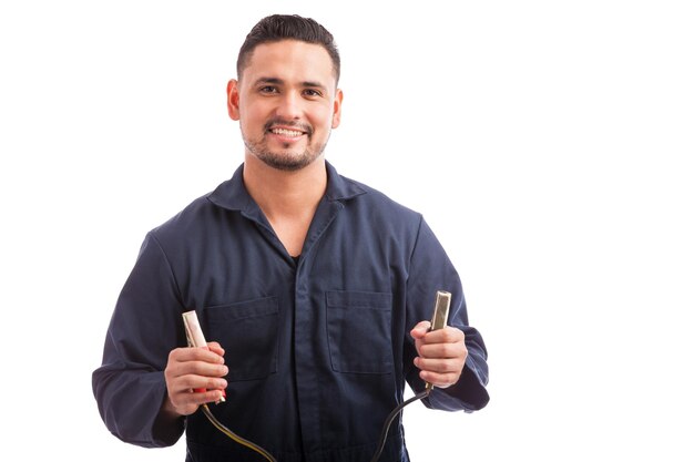 Feliz joven hispano sosteniendo un par de terminales de cable de puente en un fondo blanco