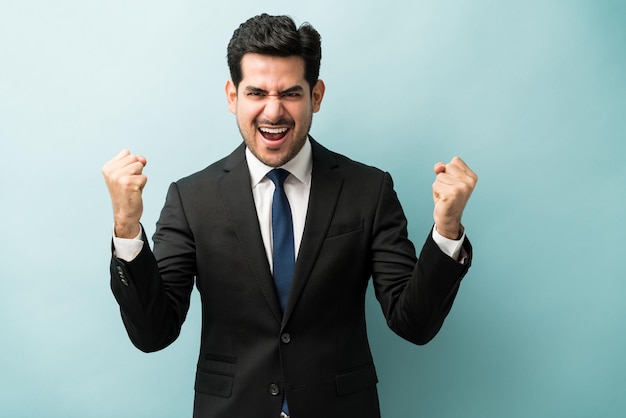 Foto gratuita feliz joven hombre de negocios con el puño cerrado disfrutando de buenas noticias contra el fondo de color