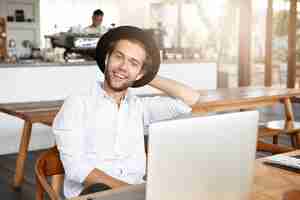 Foto gratuita feliz joven inconformista con camisa blanca y elegante sombrero con expresión de cara alegre