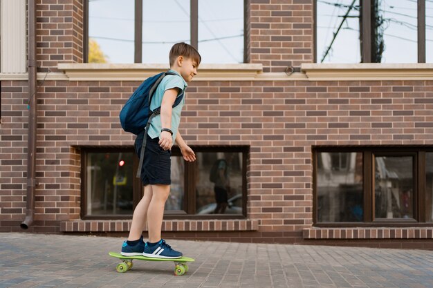 Feliz joven jugando en patineta en la ciudad, niño caucásico montando penny board