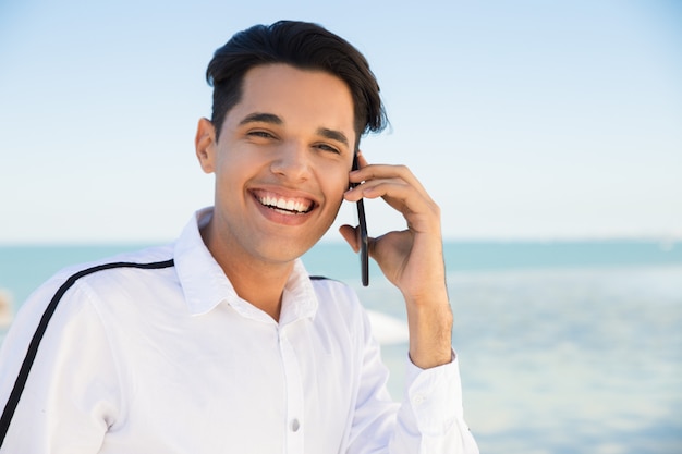 Feliz joven llamando a teléfono inteligente al aire libre