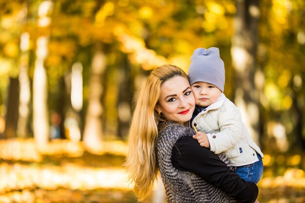 Feliz joven madre jugando con su pequeño hijo en otoño cálido sol o día de verano. Hermosa luz del atardecer en el jardín de manzanas o en el parque. Concepto de familia feliz