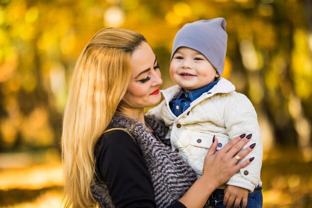 Feliz joven madre jugando con su pequeño hijo en otoño cálido sol o día de verano. Hermosa luz del atardecer en el jardín de manzanas o en el parque. Concepto de familia feliz