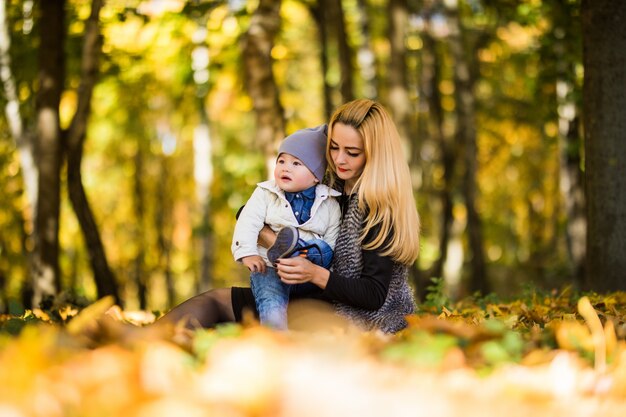 Feliz joven madre y su pequeño hijo pasar tiempo en el parque de otoño.