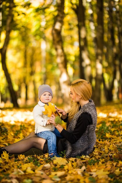 Feliz joven madre y su pequeño hijo pasar tiempo en el parque de otoño.