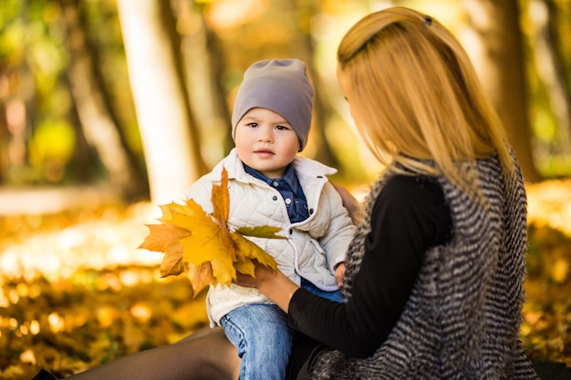 Feliz joven madre y su pequeño hijo pasar tiempo en el parque de otoño.