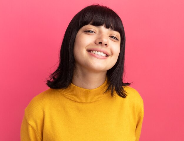 Feliz joven morena caucásica se encuentra mirando a la cámara en rosa