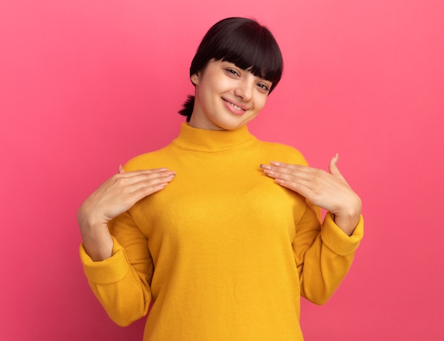 Feliz joven morena caucásica pone las manos en el pecho