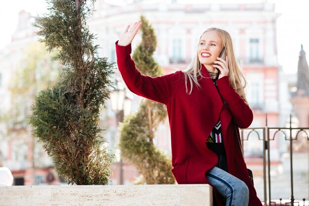 Feliz joven mujer caucásica hablando por teléfono saludando a amigos.