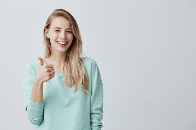 Feliz joven mujer caucásica vistiendo camisa azul de manga larga haciendo pulgar arriba signo