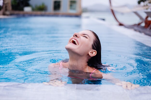 Feliz joven mujer europea delgada en bikini rosa brillante piscina azul