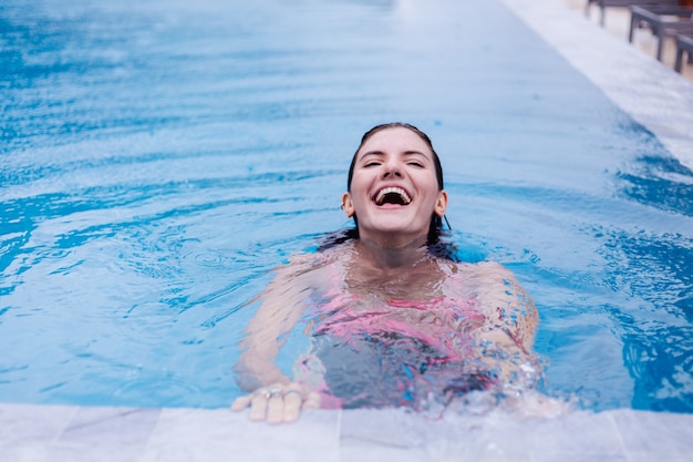 Feliz joven mujer europea delgada en bikini rosa brillante piscina azul