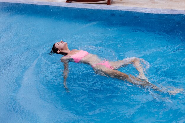 Feliz joven mujer europea delgada en bikini rosa brillante piscina azul