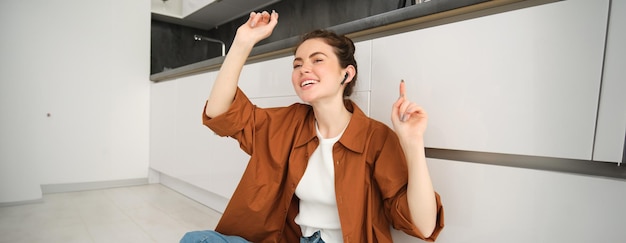 Foto gratuita feliz joven mujer moderna bailando y sentada en el suelo moviendo las manos al ritmo de la música escuchando