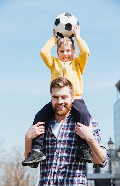Foto gratuita feliz joven padre llevando a su pequeño hijo sobre los hombros