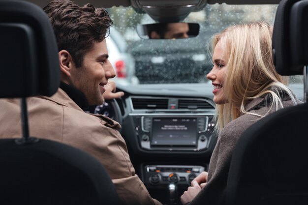 Feliz joven pareja amorosa en coche mirando el uno al otro.