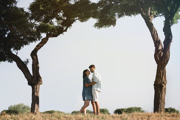 Feliz y joven pareja embarazada abrazando en la naturaleza