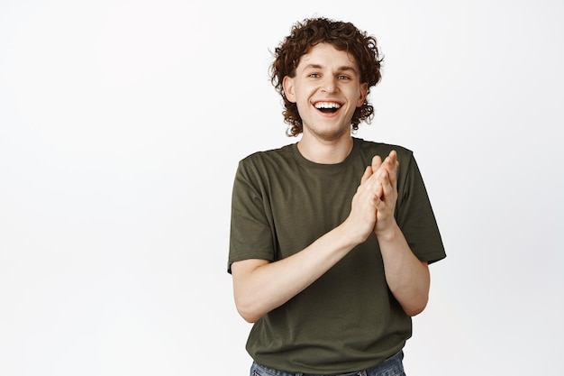 Feliz joven riendo y aplausos aplaudiendo y sonriendo alabando algo de buena posición sobre fondo blanco.