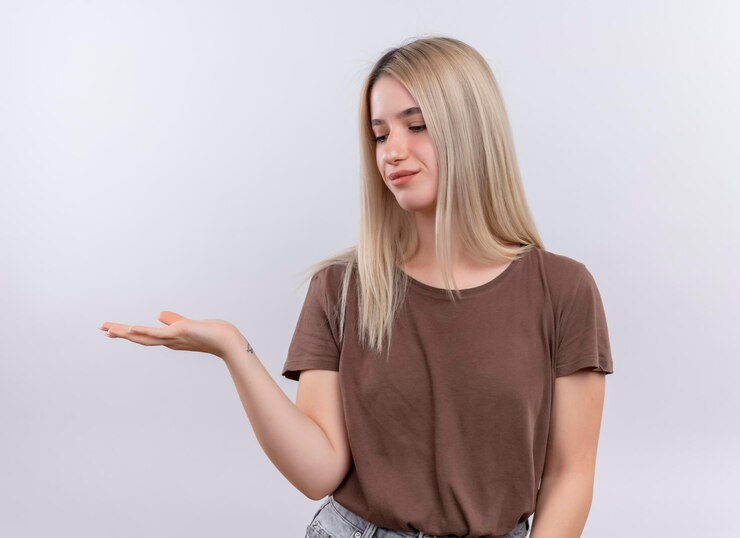 Foto gratuito feliz joven rubia mostrando la mano vacía y mirándola en un espacio en blanco aislado
