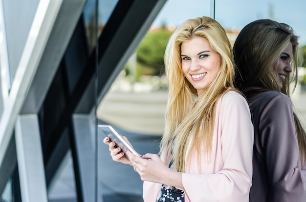 Feliz joven rubia sonriendo con tableta en la calle