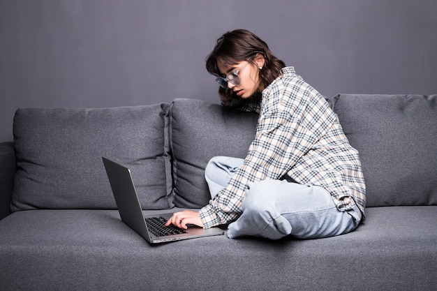 Feliz joven sentada en el sofá usando su computadora portátil en casa en la sala de estar