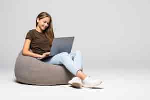 Foto gratuita feliz joven sentada en el suelo con ordenador portátil en la pared gris