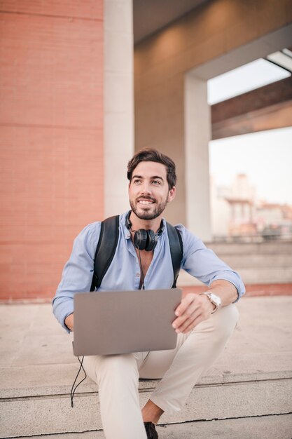 Feliz joven sentado en la escalera con la computadora portátil