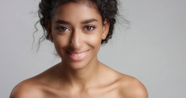 Foto gratuita feliz joven serena con hermosa piel oliva y cabello rizado piel ideal y ojos marrones en el estudio