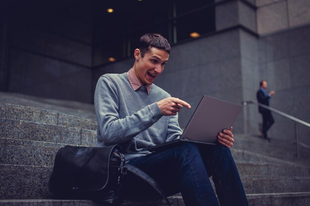 Feliz joven sonriente con laptop en un centro de la ciudad.