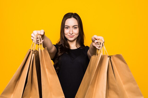 Feliz joven sosteniendo bolsas de la compra en una pared amarilla