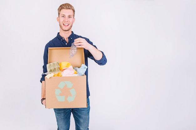 Foto gratuita feliz joven sosteniendo la caja de cartón llena de basura con el icono de reciclaje