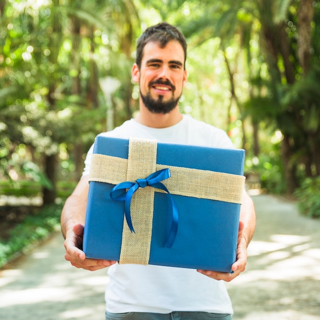 Feliz joven sosteniendo la caja de regalo azul