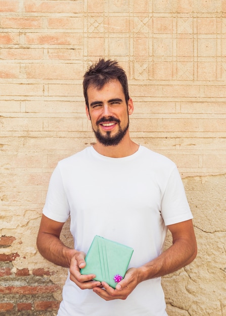 Foto gratuita feliz joven sosteniendo la caja de regalo en frente de la antigua muralla