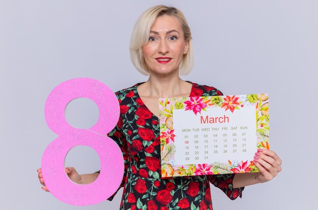 Feliz joven sosteniendo el calendario de papel del mes de marzo y el número ocho sonriendo alegremente celebrando el día internacional de la mujer de marzo