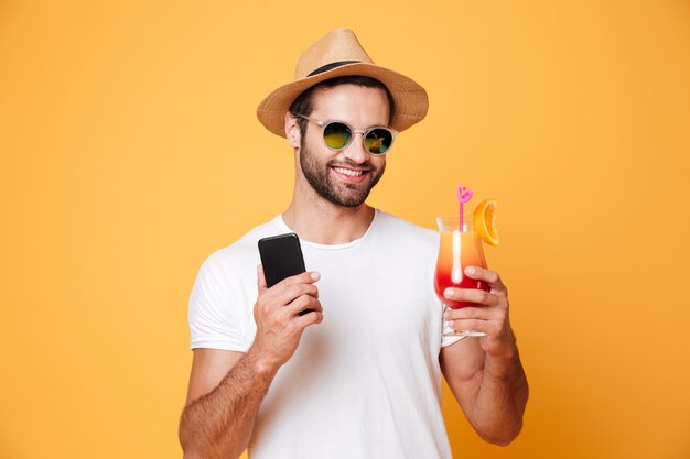 Feliz joven sosteniendo teléfono móvil y cóctel