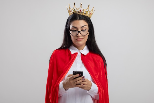 Foto gratuita feliz joven superhéroe caucásica con gafas y corona con teléfono móvil aislado sobre fondo blanco con espacio de copia