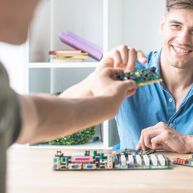 Feliz joven técnico informático masculino tomando el circuito de hardware de su amigo