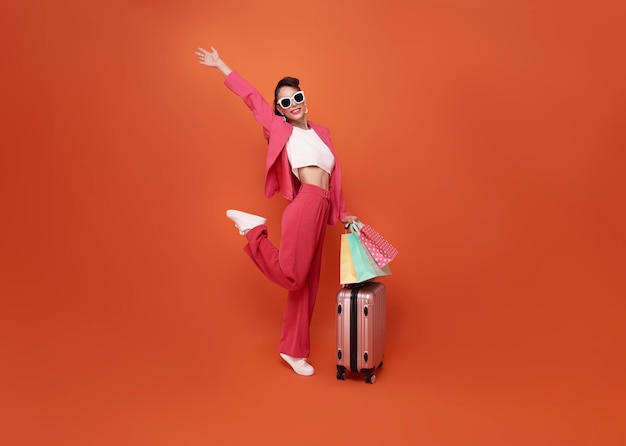 Feliz joven viajera arrastre equipaje y bolsa de compras aislada en el fondo del espacio de copia naranja