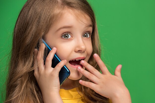 Feliz jovencita de pie, sonriendo con teléfono móvil sobre estudio verde de moda