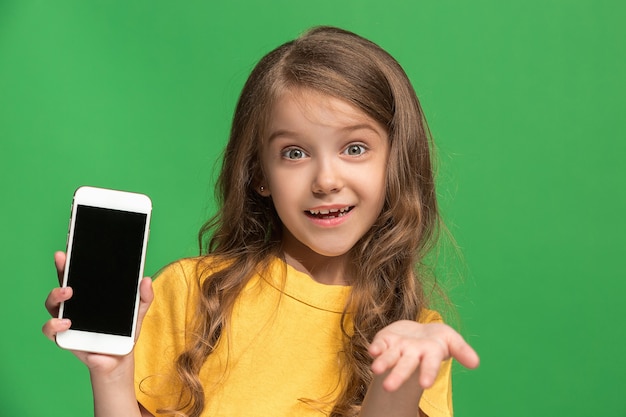 Feliz jovencita de pie, sonriendo con teléfono móvil sobre estudio verde de moda.