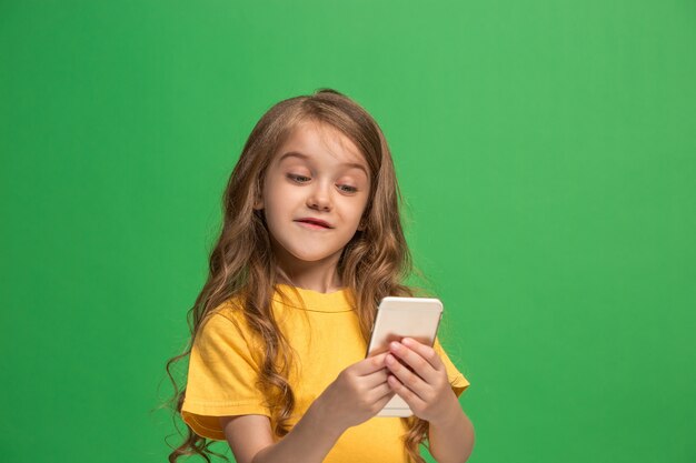 Feliz jovencita de pie, sonriendo con teléfono móvil sobre fondo de estudio verde de moda.