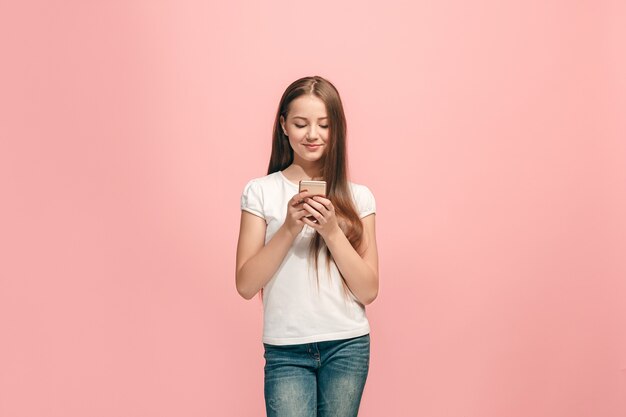 Feliz jovencita de pie, sonriendo con teléfono móvil sobre la pared de moda estudio rosa