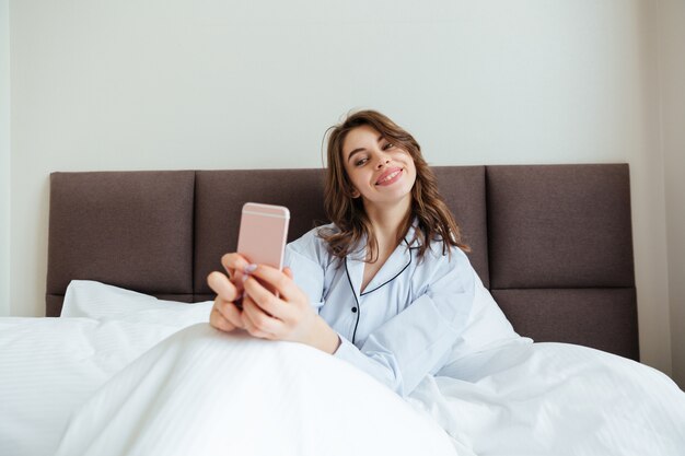 Feliz jovencita vestida con pijama hacer selfie.