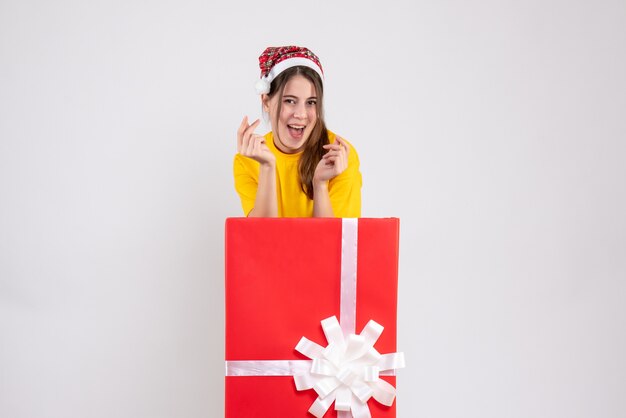 Feliz linda chica con gorro de Papá Noel de pie detrás de un gran regalo de Navidad en blanco