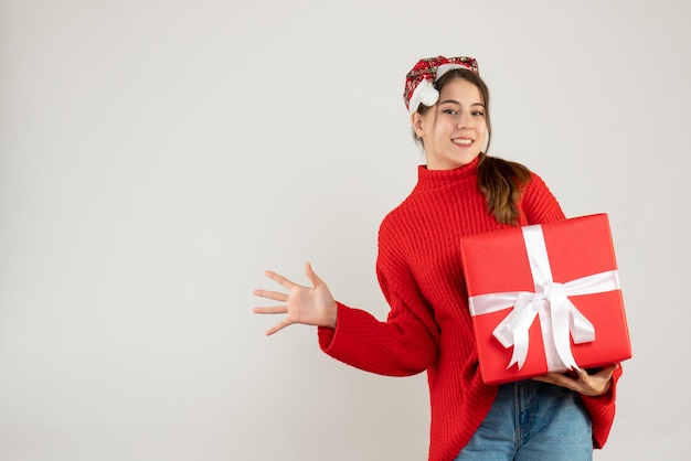 Feliz linda chica con gorro de Papá Noel con regalo y abrir su mano de pie sobre blanco